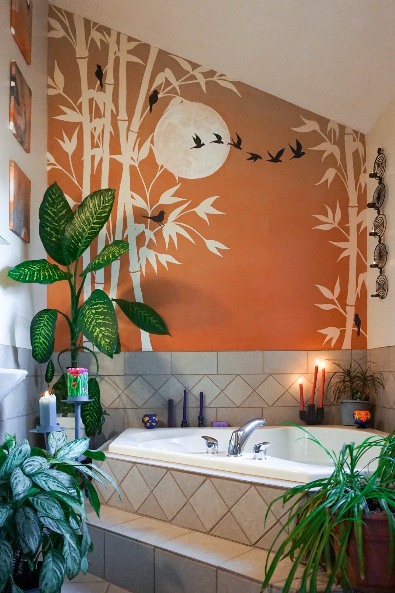 Bathroom mural of a copper moon and birds in flight over white bamboo, wrapping the wall above a corner tub.